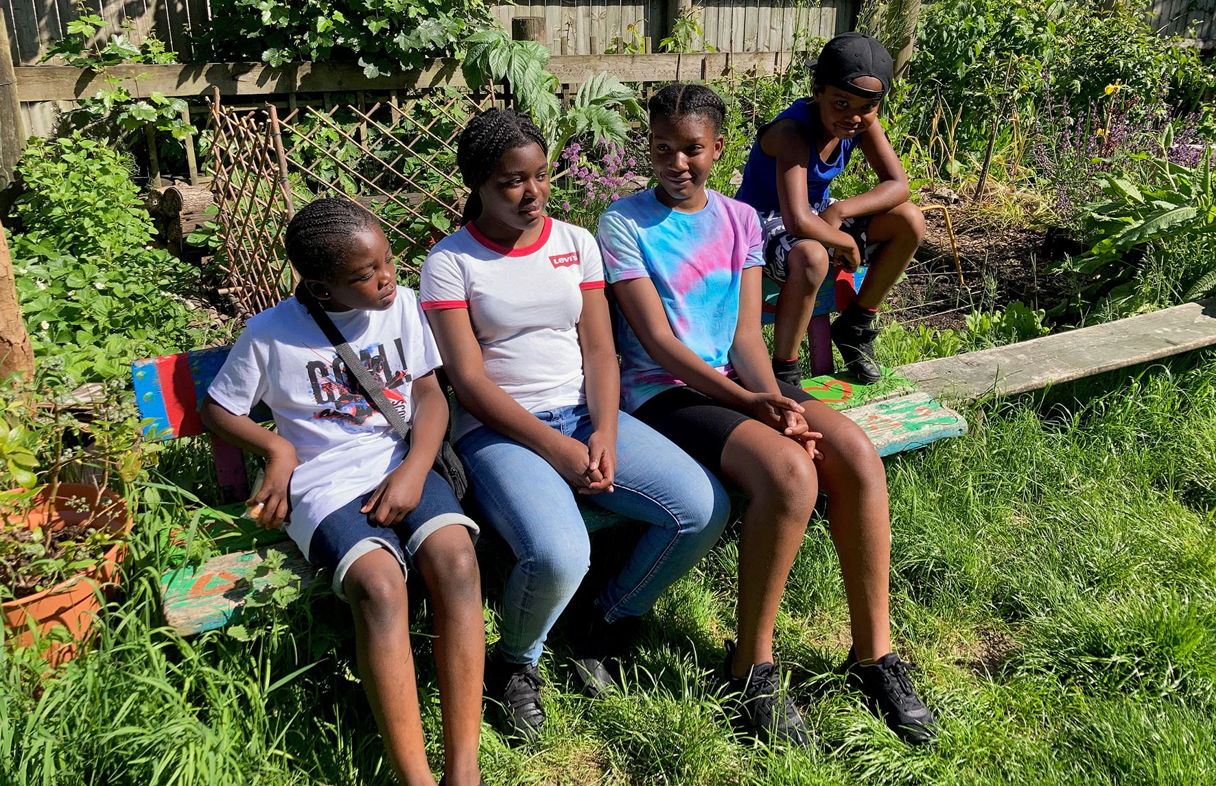 Four African-Caribbean heritage children / teenagers seated on a wooden bench outside in St Paul's Adventure playground